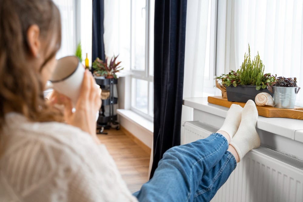 Girl holding a cup with feet placed on a radiator